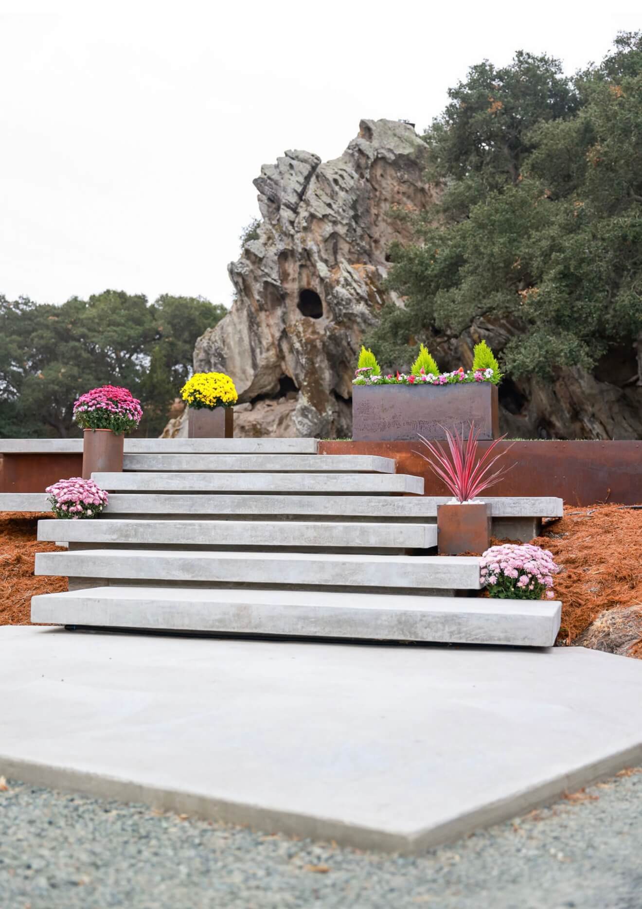A display of handcrafted Corten steel planters of various shapes and sizes, arranged along concrete steps in a landscaped outdoor setting.