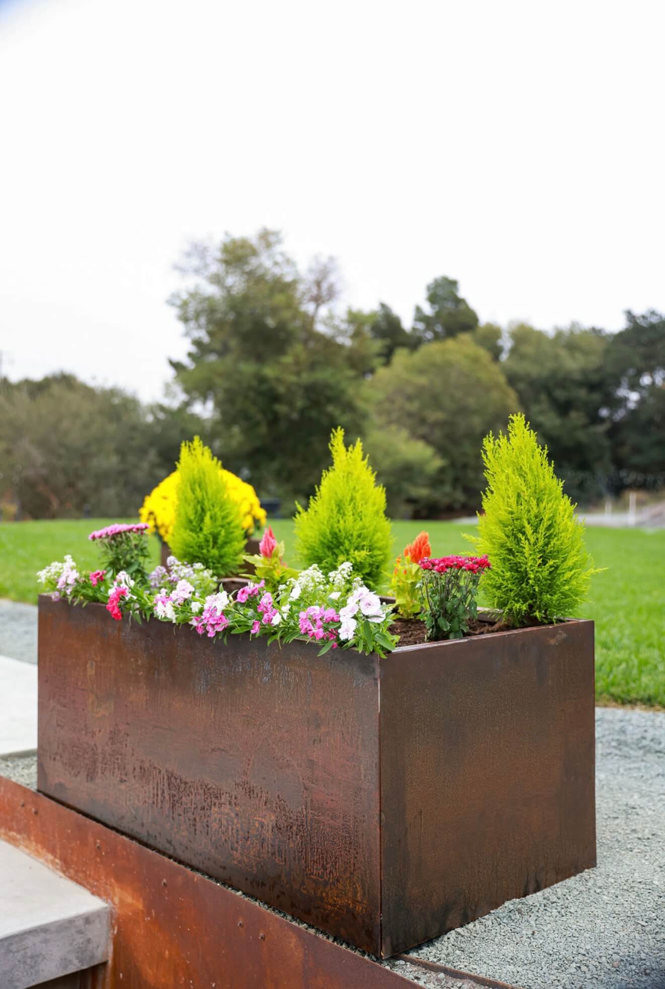A rectangular Corten weathering steel planter featuring bright green and pink plants in a modern outdoor space.